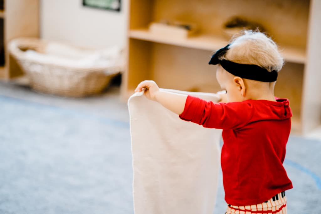 toddler rolls out a mat to begin her work in a montessori classroom